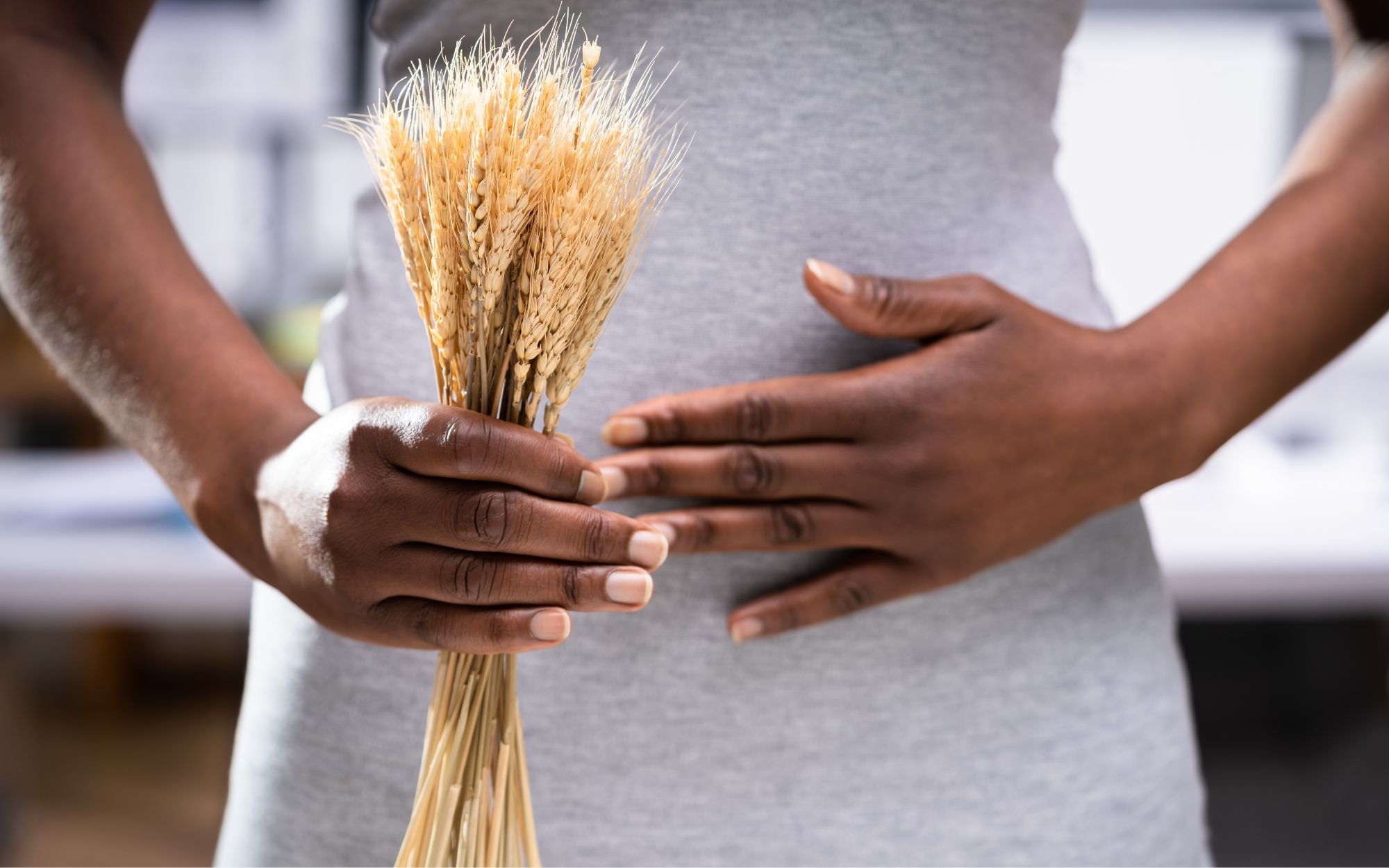 Person with hand on stomach and holding a wheat in other hand